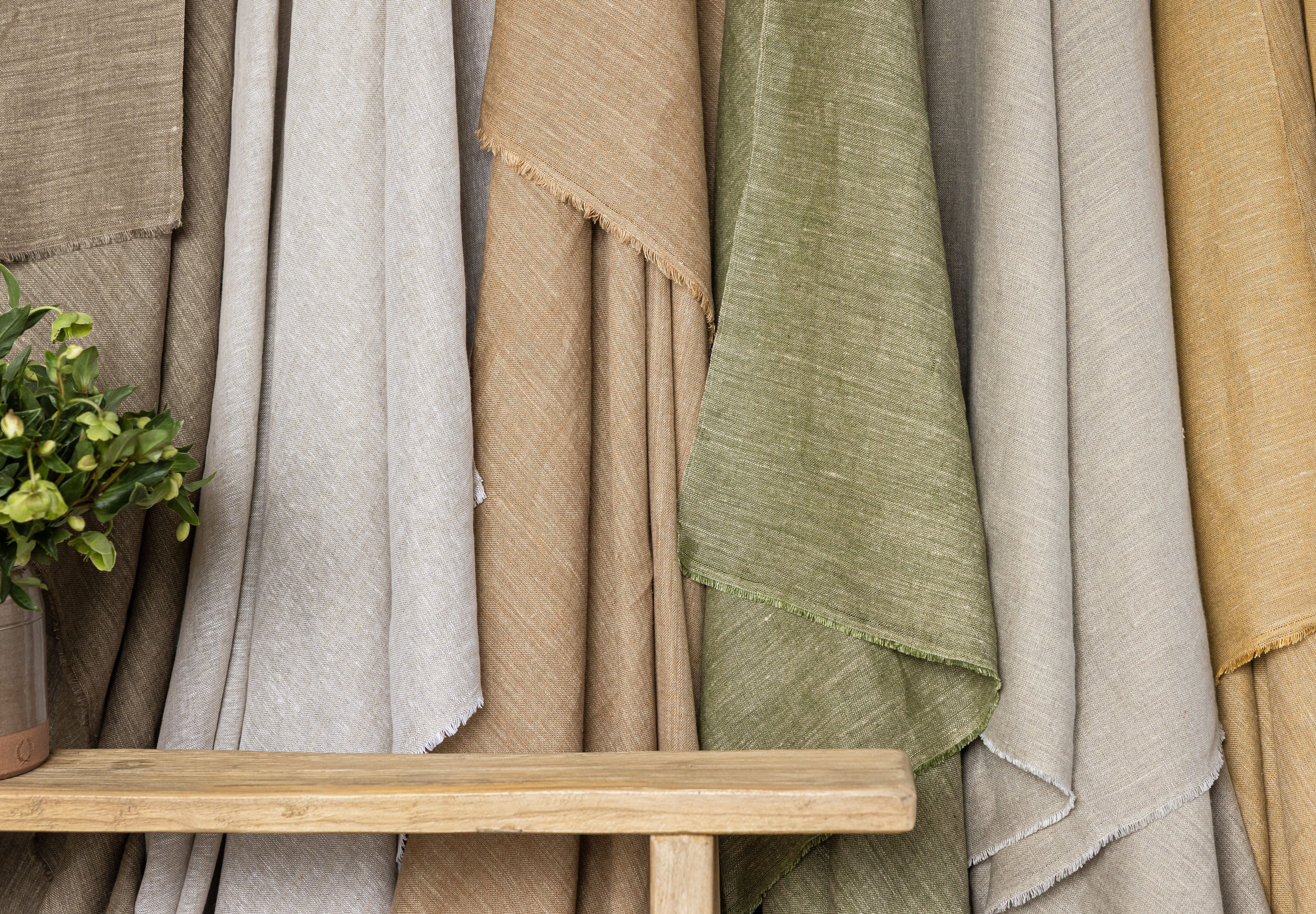 Collection of textured fabrics in various colors with a wooden bench and plant.