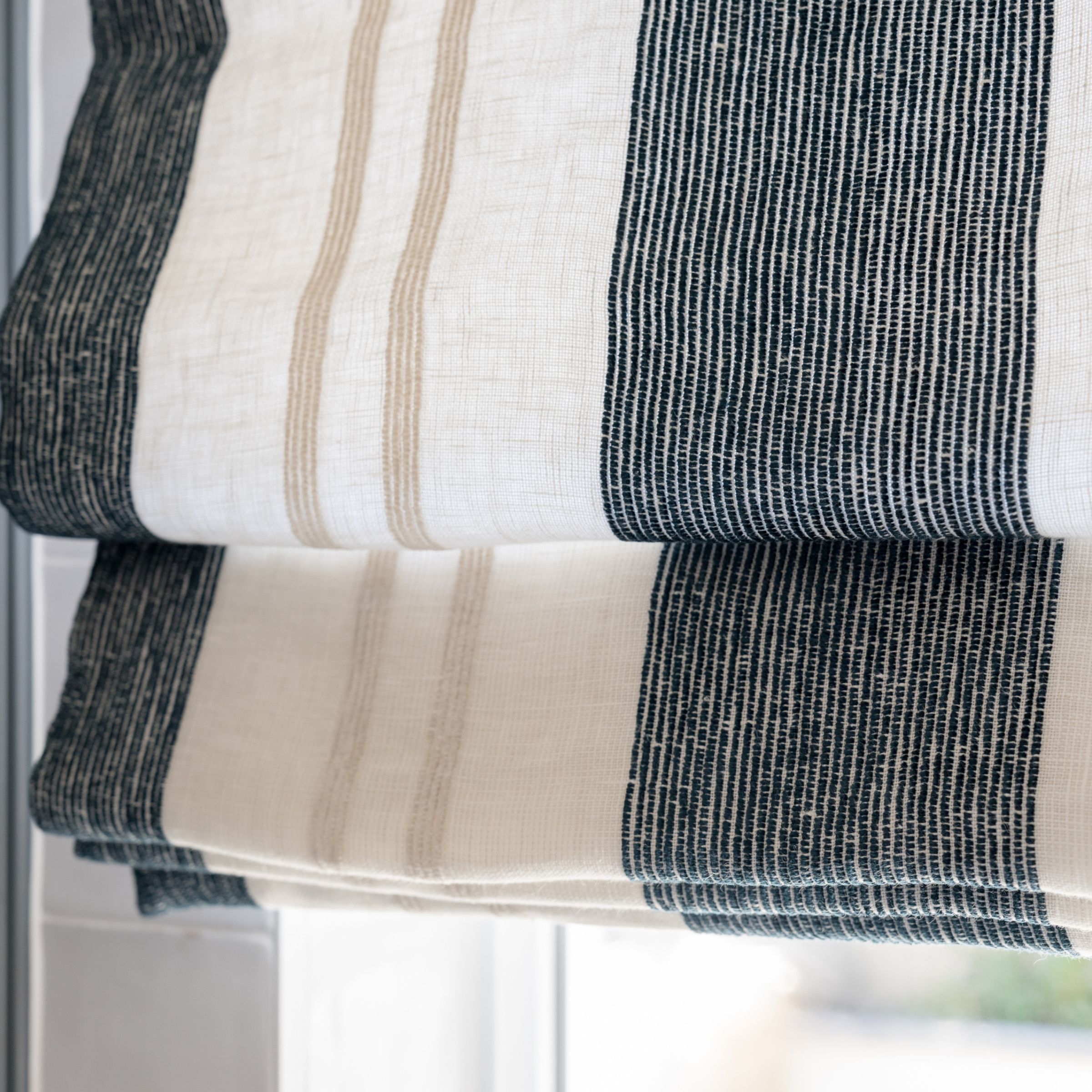 Striped roman shade with blue, beige and white pattern.