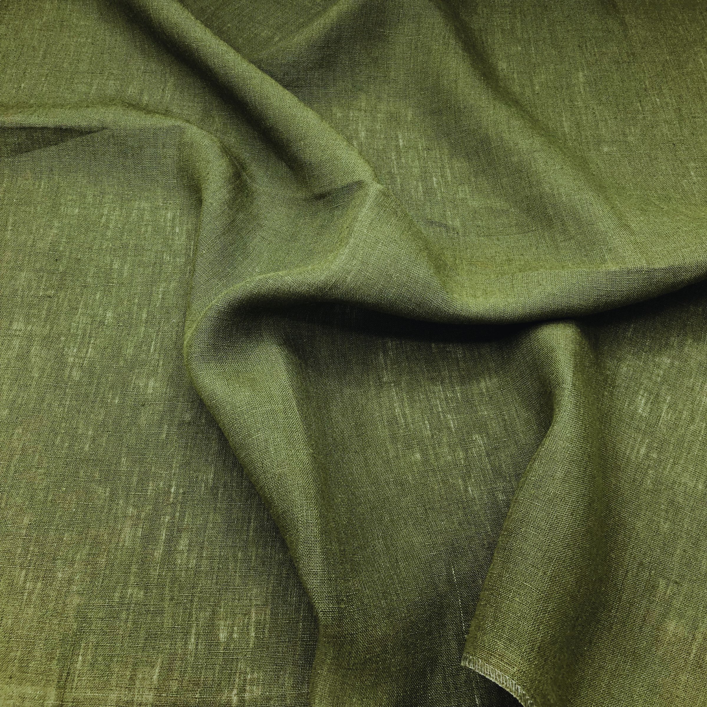 Close-up of dark green fabric with a plain matte weave and large wavy folds