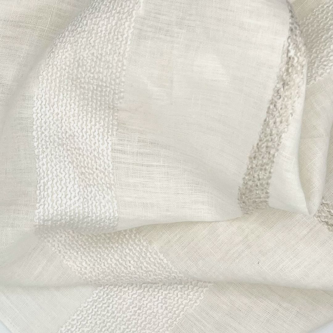 Off-white plain fabric adorned with textured white and gray stripes sporting large wavy folds.